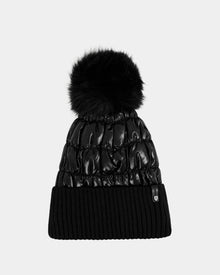 The Rudsak LANYA - L423514 Metallic Black is a black winter hat featuring a shiny quilted pattern, a large faux fur pom-pom, and a ribbed knit fold-over cuff in wool blend, shown on a plain light gray background.