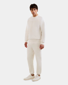 A man faces forward in an all-white outfit, wearing Rudsak's MAXTON - U525007 Vanilla M sweatshirt and unisex jogger pants with sneakers, set against a plain white background.