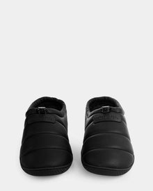 The Rudsak MILTON - M225504 Black men’s quilted slippers feature a cozy faux-shearling lining, rounded toes, and a small logo patch on the front, shown against a plain light background.