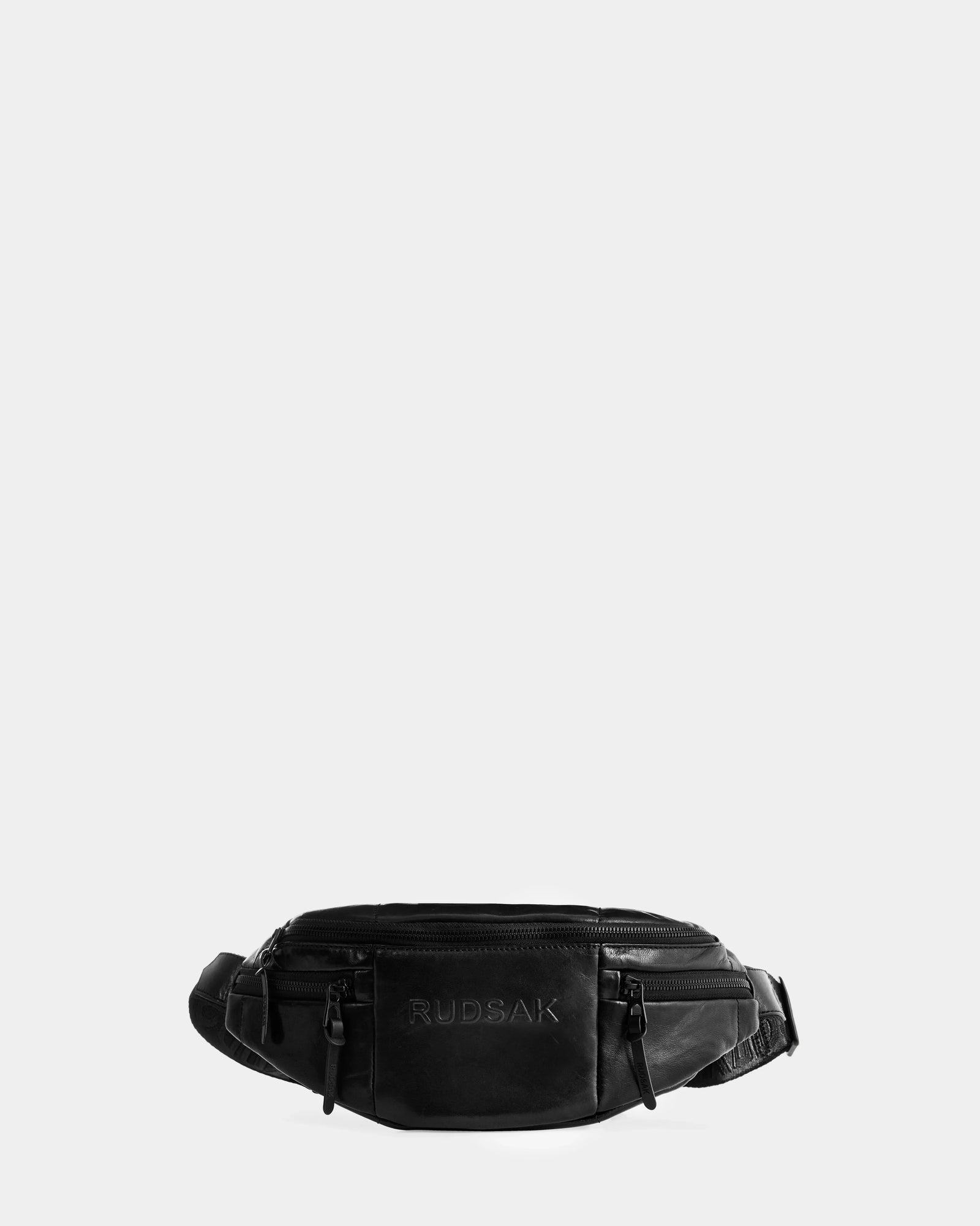 The Rudsak RILONI L - U325002 Black is a unisex leather belt bag with multiple zippered compartments and an adjustable strap, shown on a light grey background. This versatile design easily doubles as a crossbody for hands-free use.