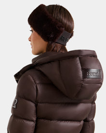 A woman is shown from the back and side wearing the Rudsak SANDIE - L425552 Espresso puffer jacket with matching faux fur headband, featuring Rudsak patches, against a plain light background.