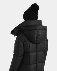 A person shown from the back against a plain light background is wearing the Rudsak SASHA - 8125686 Black women’s long down puffer coat with a removable hood and a black knit beanie with a pom-pom.