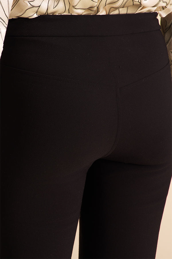 Person wearing black pants and a patterned top on a beige background | Exclude