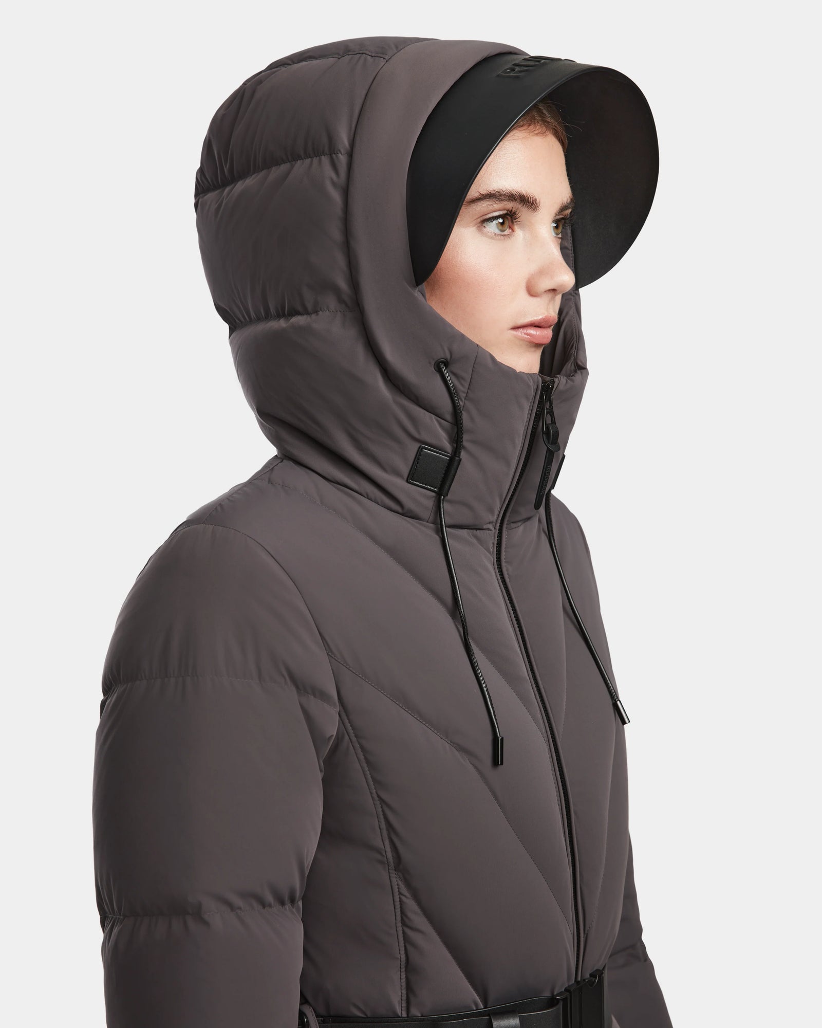 A woman in the Rudsak ENZAH - 8124692 Grey down puffer jacket with black drawstrings and a black brimmed hat is shown in profile against a plain white background.