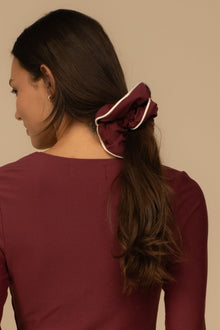 Maroon chunky scrunchie with cream piping detail worn in dark hair.