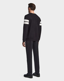 A man faces away wearing the Rudsak OMAR - 6523507 Black men’s knit sweater with two white stripes on each sleeve, paired with black pants and shoes, against a plain light gray background.