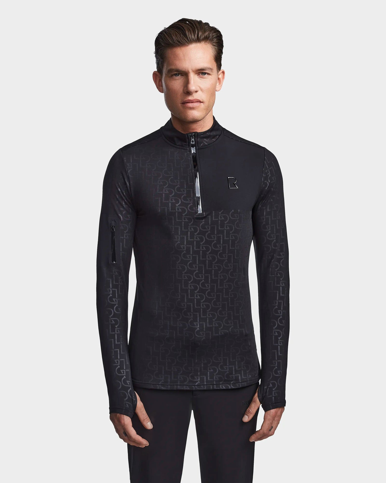A man faces forward wearing the Rudsak WARREN - 6523502 Black Pattern men’s fitted stretch top with a zip-front mock neck and subtle geometric design, standing against a plain background with hands relaxed by his sides.