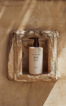 Front view of Dripping In Opulence shower oil (pump dispenser) showcasing N°16 label in a sunlit stone niche