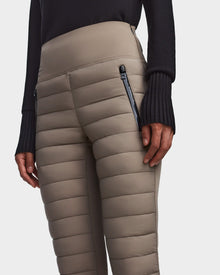 A person wears Rudsaks ARIL M - 8522514 Cement quilted pants with horizontal stitching and zippered pockets, paired with a long-sleeve black top. Only the torso and upper legs are visible.