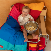 Baby sitting on top of STATE Bags Redwood Sleeping Bag Rainbow Chevron eating popcorn