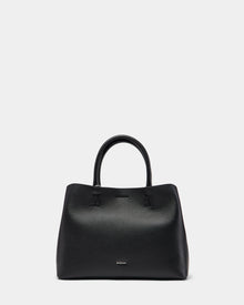 The CATIRA S - 8325006 Black by Rudsak is a structured black pebble leather tote with two handles, minimal seams, and a removable shoulder strap. The Rudsak logo appears in small silver lettering near the bottom center on a plain white background.