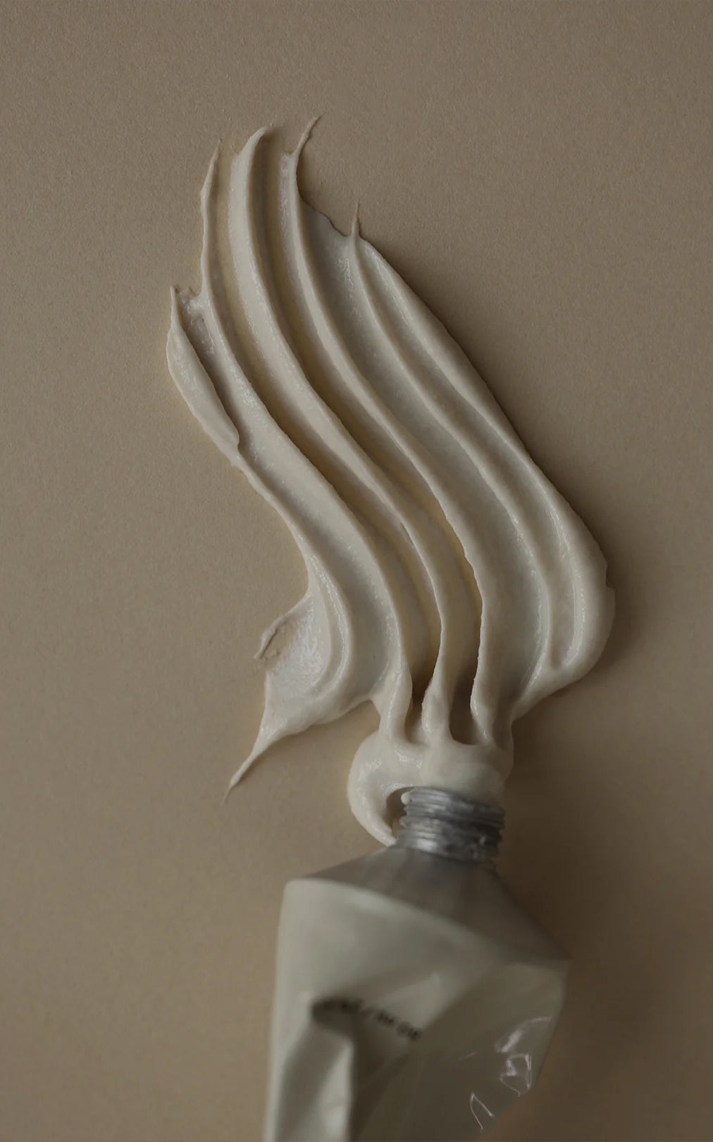 Close-up of The Polish tube showcasing beige cream fanned into textured ridges on a tan background