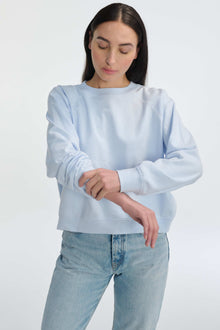 Woman wearing a light blue sweatshirt and jeans on a white background
