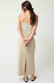 Woman wearing a beige strapless top with a matching beige skirt on a light grey background