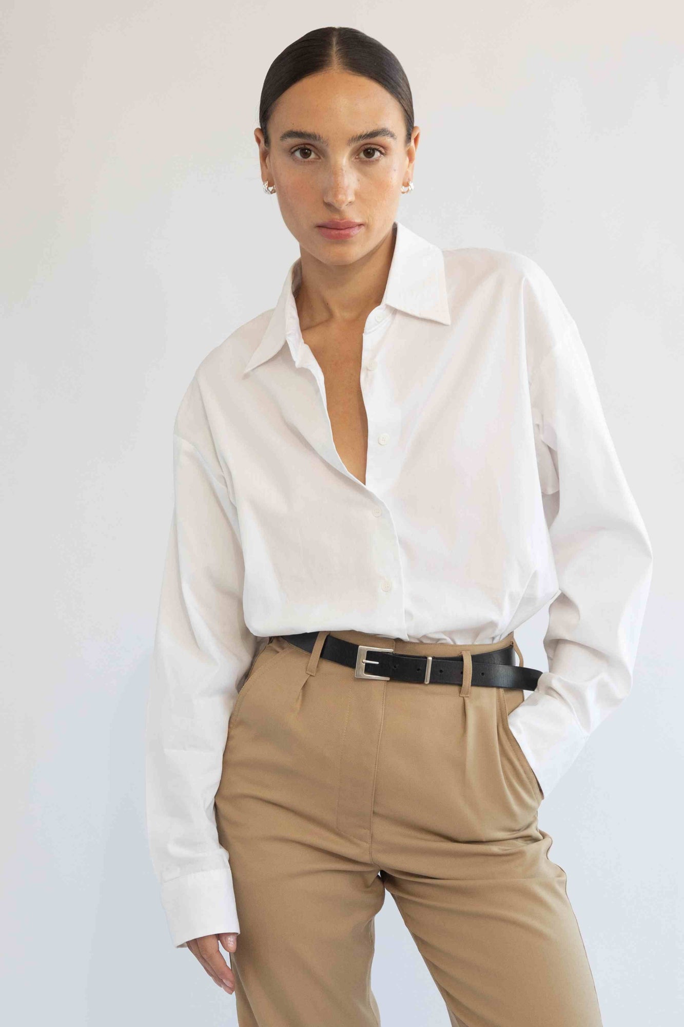 Woman wearing a white shirt and beige pants against a plain background