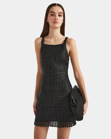 A woman with straight brown hair models the Rudsak NATALIA - 8524045 Black, an elegant handwoven sleeveless dress, paired with a matching black clutch, against a plain white background.