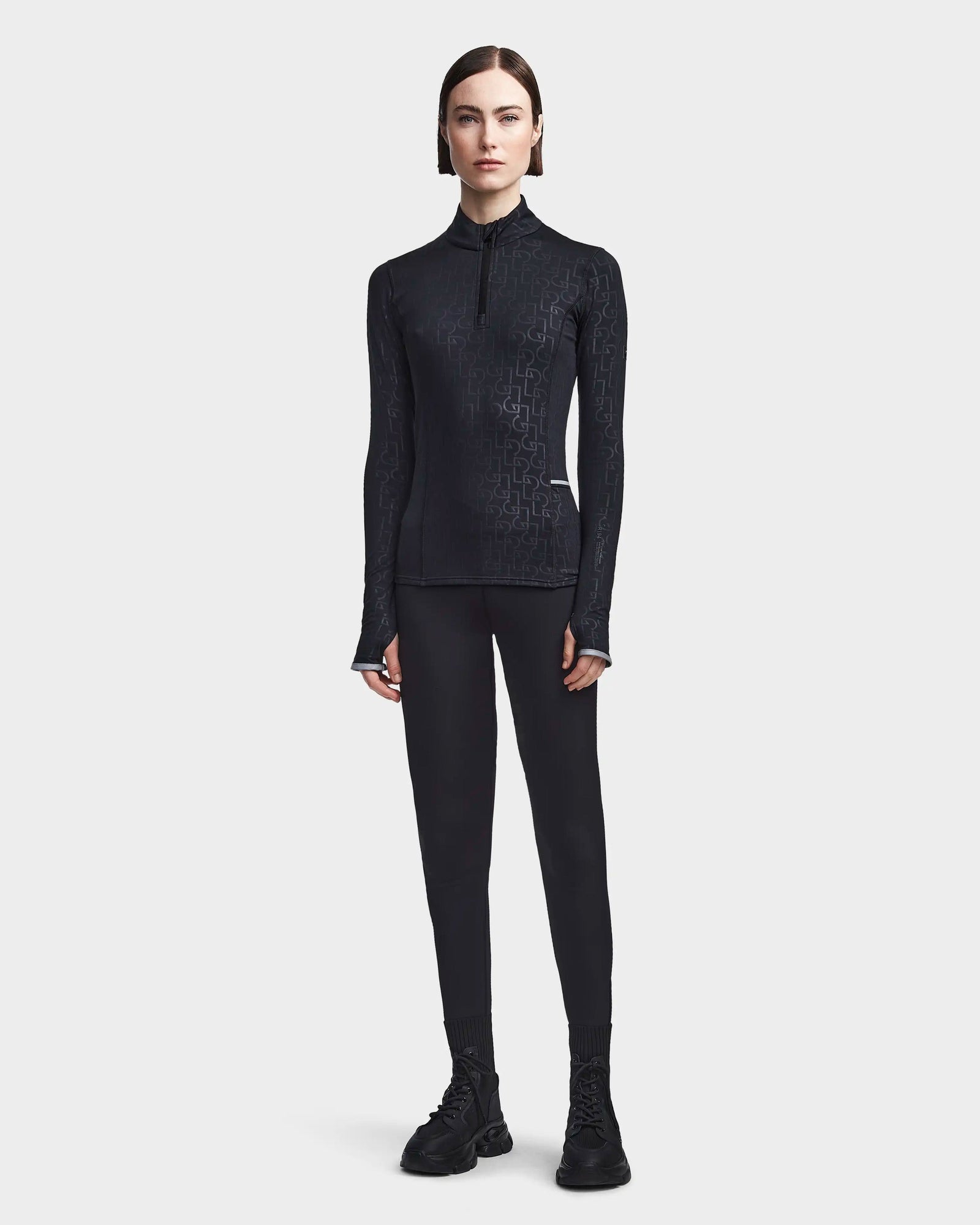 A person with short brown hair faces forward, wearing the Rudsak SIRE - 8523531 Black Pattern ski top, black leggings, and black lace-up boots against a plain light background—ideal for cold weather fashion.