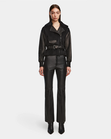 A woman faces forward in a Rudsak HALA - 8124521 Black fall jacket with a belted waist, paired with black leather pants and pointed-toe boots, set against a plain white background.