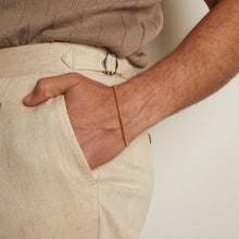 Person wearing a gold bracelet with beige pants and shirt.