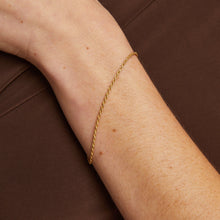 Model. Gold bracelet on a person's wrist against a brown background
