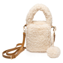 Eugenia Kim Tate Bag in Cream. A cozy faux shearling bucket bag featuring a plush handle, adjustable tan leather crossbody strap, and playful pom-pom detail. Perfect for adding warmth and texture to any winter outfit.